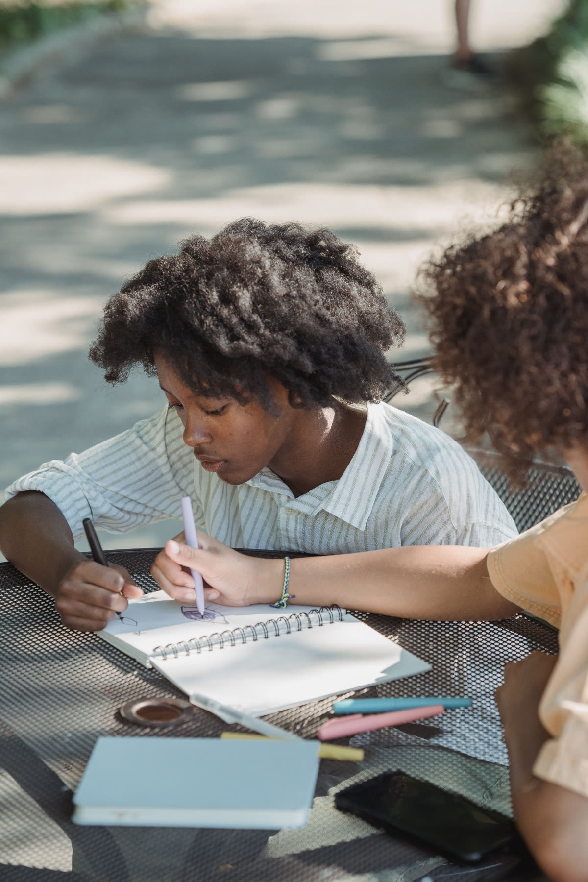 A teen and a mentor drawing together at an outdoor table